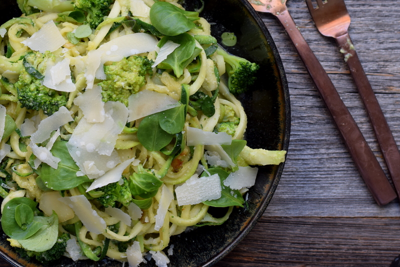 Bovenaanzicht: Zwart bord met courgetti met cashewsaus en broccoli rechts bestek