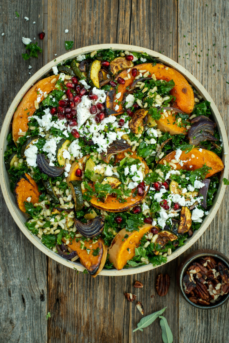 Bovenaanzicht van een ronde schaal gevuld met een salade van geroosterde pompoen met kamut, boerenkool en feta; op een houten ondergrond.