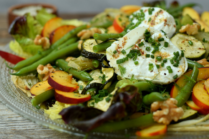 Zijaanzicht een glazen bord met groen-gele salade met mozzarella en walnoten
