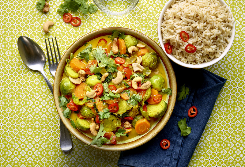 Bovenaanzicht: een bord met curry met spruitjes en boerenkool rechts een kommetje rijst