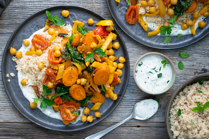 Bovenaanzicht: links een bord couscous met currygroenten en yoghurtsaus rechts een potje saus en couscous apart