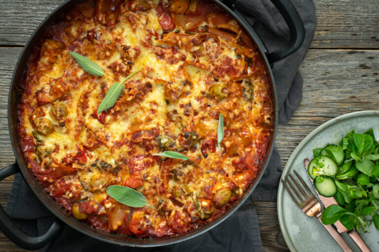 Bovenaanzicht van een gegratineerde lasagne, in een zwarte, ronde ovenschotel, op een houten ondergrond.