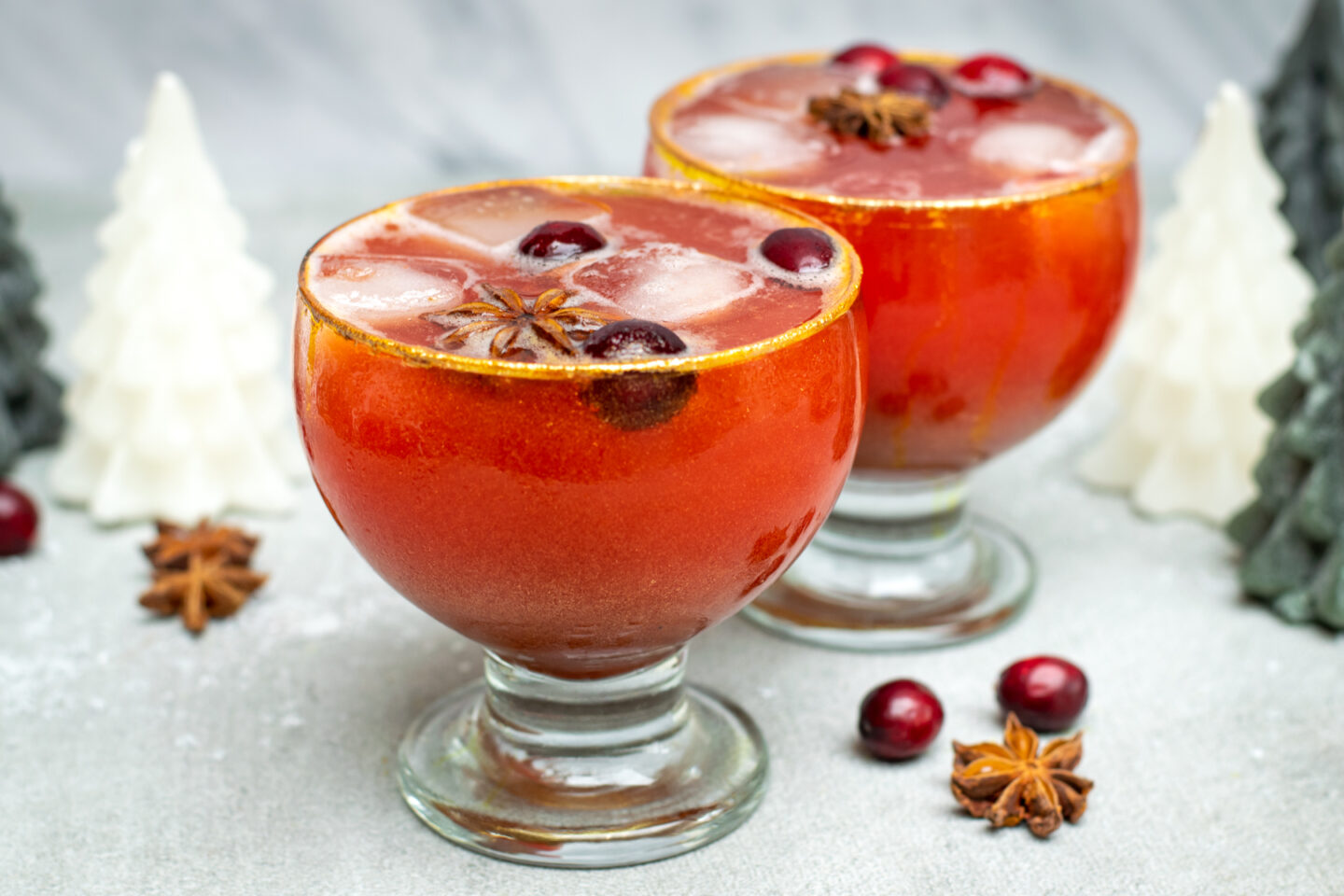 Twee bolvormige glazen gevuld met een oranjerode appel-cranberrymocktail, afgewerkt met gouden glitter.