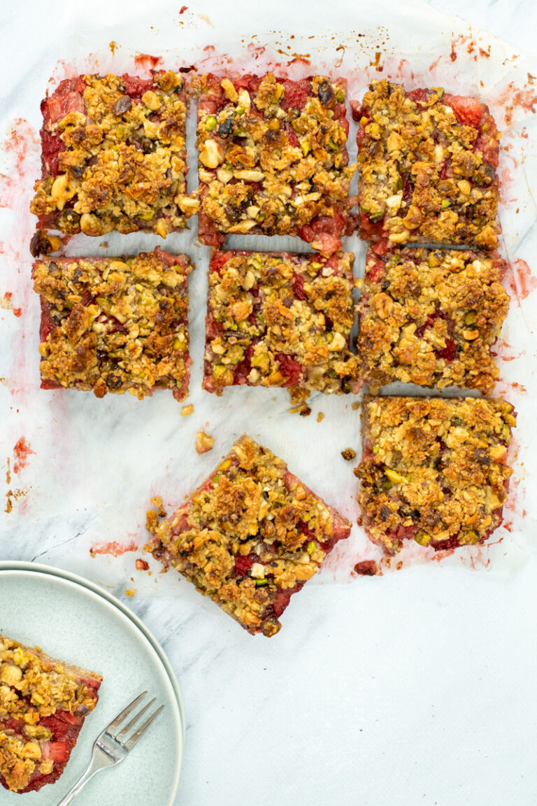 Bovenaanzicht van aardbei-crumble gebak, in vierkantjes gesneden, op een witte marmeren ondergrond.