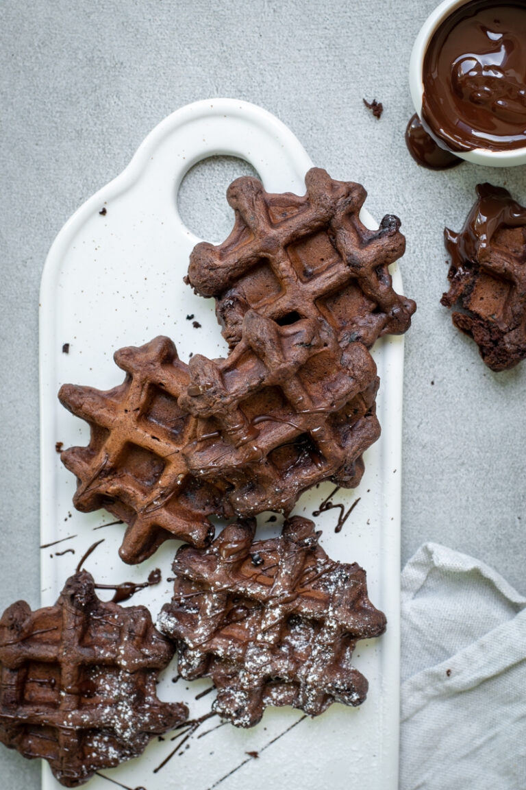 Bovenaanzicht van 5 chocoladewafeltjes, op een wit keramieken plankje, op een lichtgrijze stenen achtergrond.
