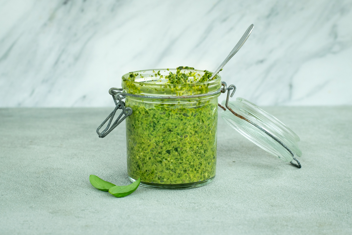 Zijaanzicht van een bokaaltje pesto op een lichtgrijze stenen achtergrond.