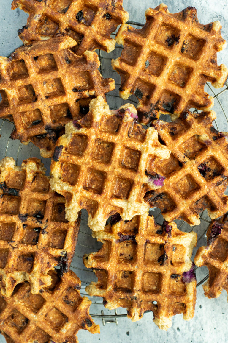 Bovenaanzicht van Cottagecheese wafels met vanille en bessen, op een metalen rooster op een lichtgrijze ondergrond.