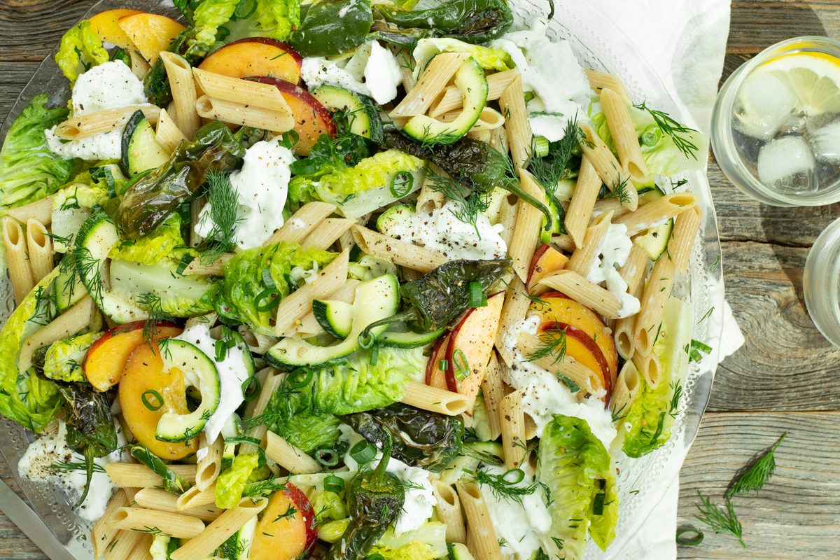 Bovenaanzicht van een pastasalade met perzik, gebakken padronpepertjes, buffelmozzarella, lente-ui en dille.