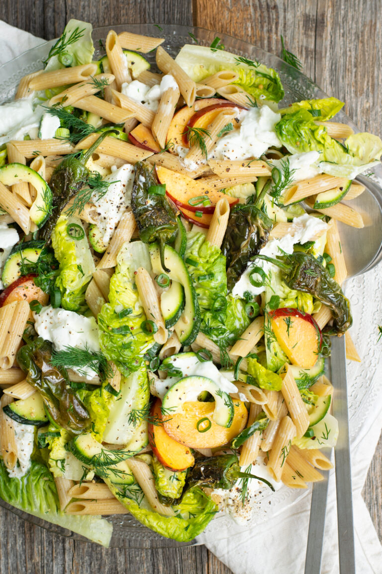 Bovenaanzicht van een pastasalade met perzik, gebakken padronpepertjes, buffelmozzarella, lente-ui en dille.