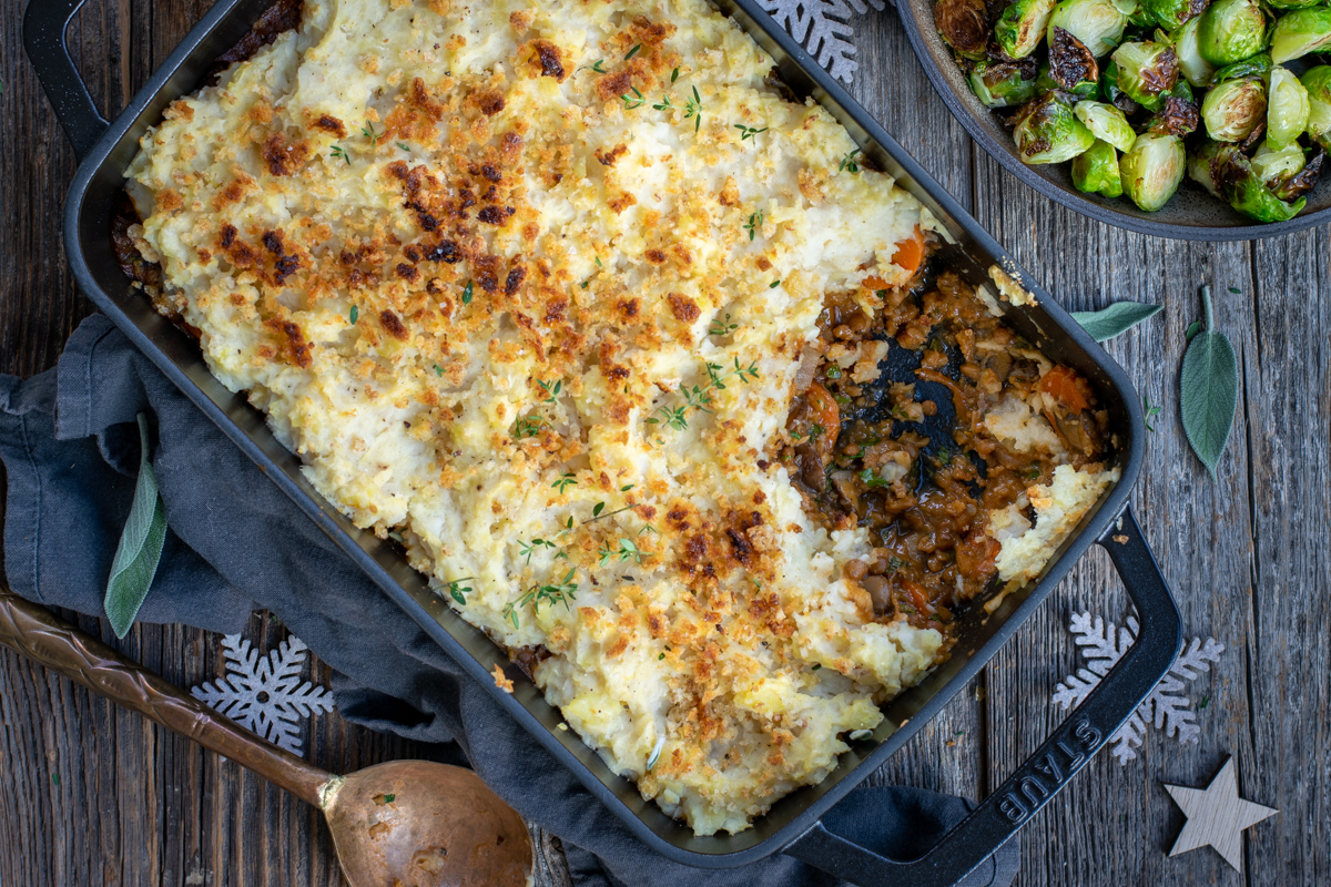 Bovenaanzicht van een ovenschotel met puree en een champignonvulling, op een ruwe houten ondergrond, met wat kerstdecoratie.