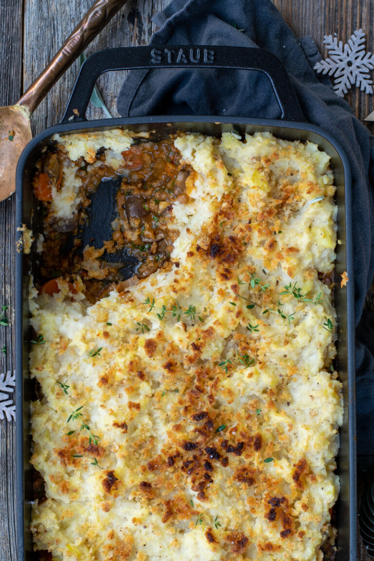 Bovenaanzicht van een zwarte ovenschotel met puree en een champignonvulling, op een ruwe houten ondergrond.