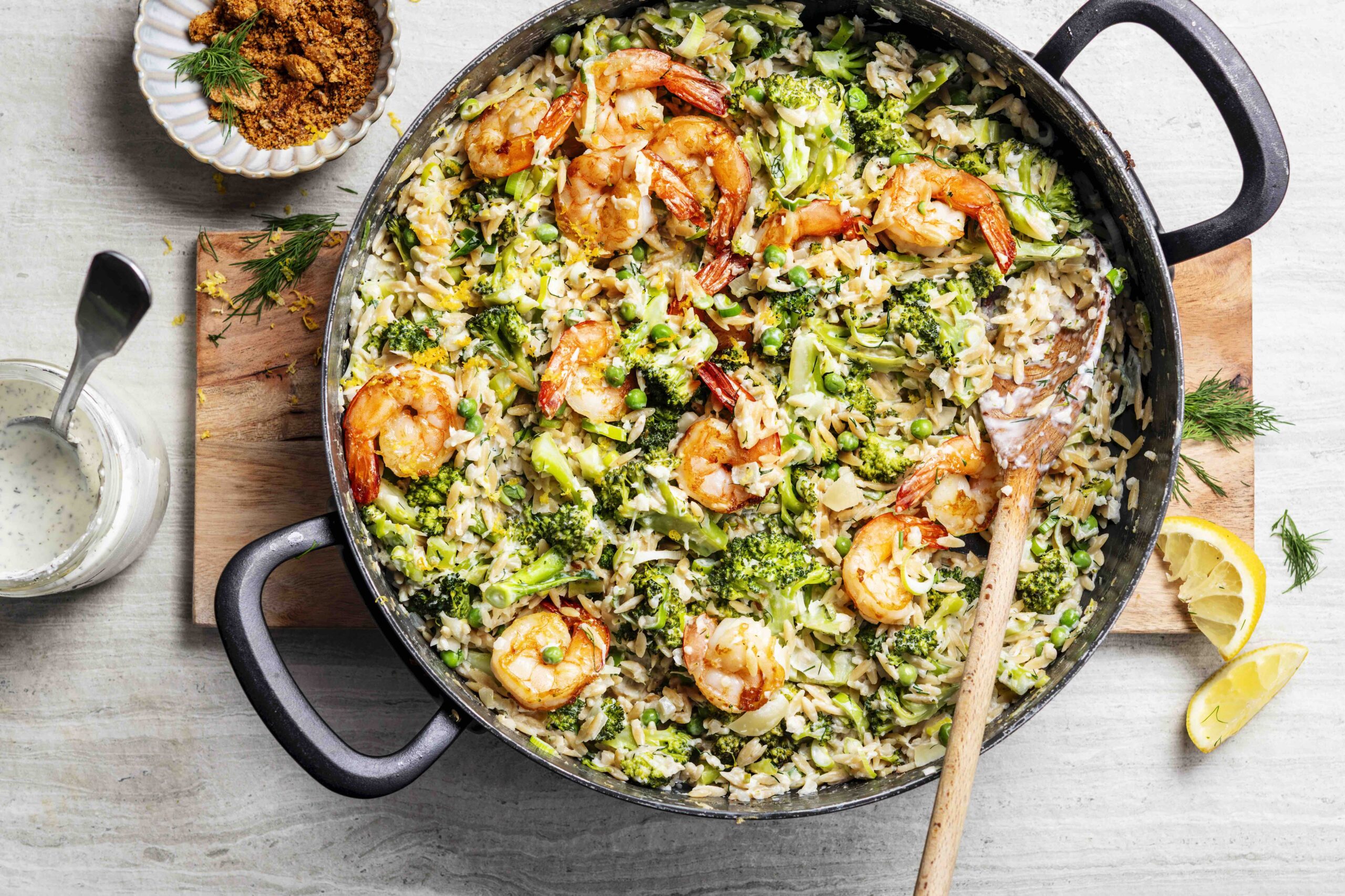 Bovenaanzicht van een stoofpan met broccoli-orzotto met scampi's, citroen en fetasaus.
