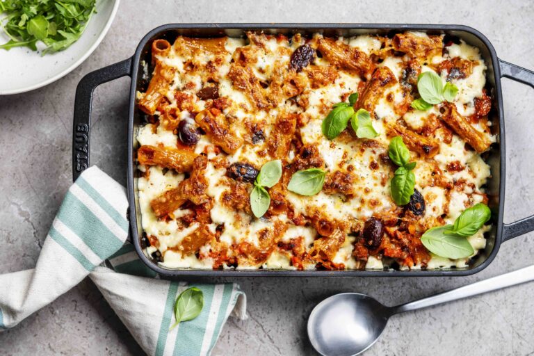 Bovenaanzicht van een gegratineerde pastaschotel met gehakt en kerstomatensaus, in een zwarte, rechthoekige ovenschaal, op een lichtgrijze ondergrond.