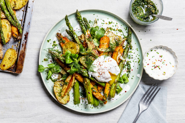 Bovenaanzicht geroosterde krieltjes, asperges en wortel met een gepocheerd ei, romige cottagecheesese-saus en kruidenolie