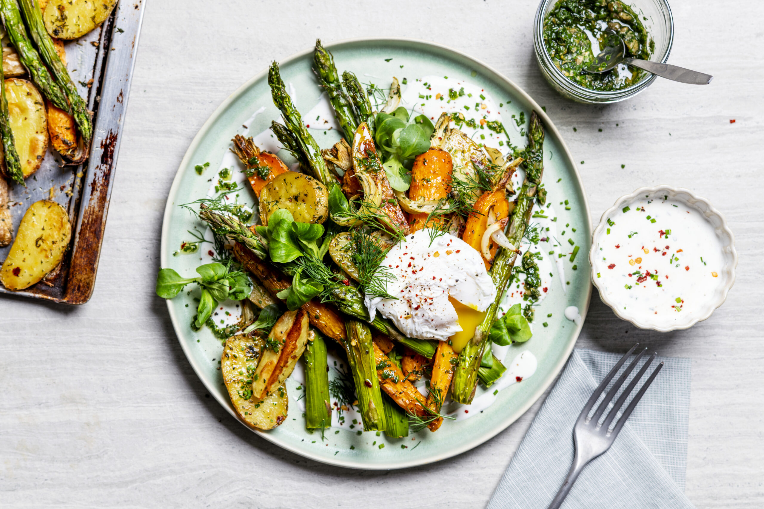 Bovenaanzicht geroosterde krieltjes, asperges en wortel met een gepocheerd ei, romige cottagecheesese-saus en kruidenolie